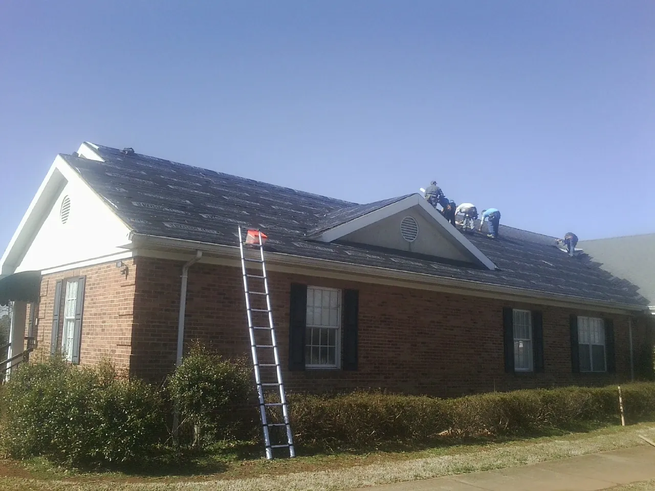 Crew tearing shingles off a brick ranch roof with a ladder set — Emergency Roof Repair work by our crew in Beyer
