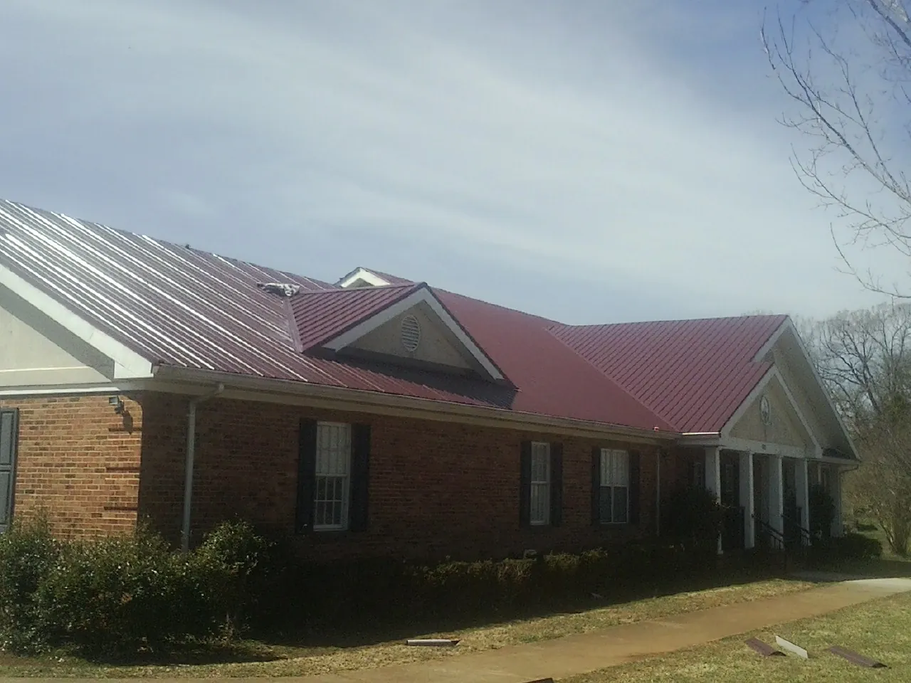 Red metal roof with gabled entries on a long brick building, from a Hail Damage Roof Repair job in Beyer