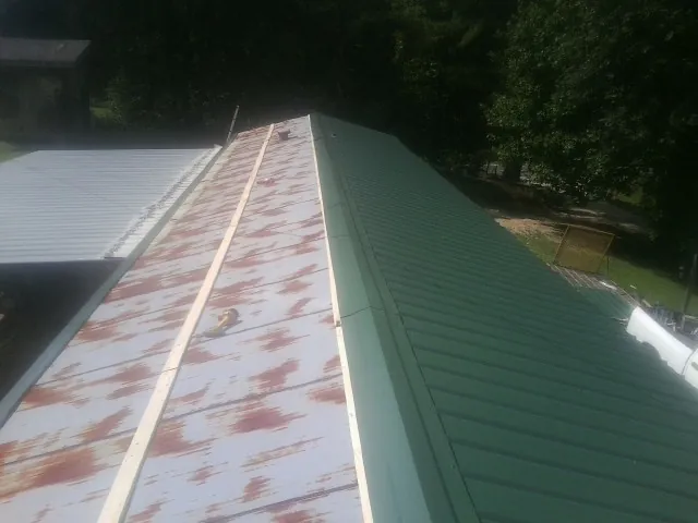 Old rusted panels beside newly installed green metal roofing — Wind Damage Roof Repair by Roofing Brothers in Beyer