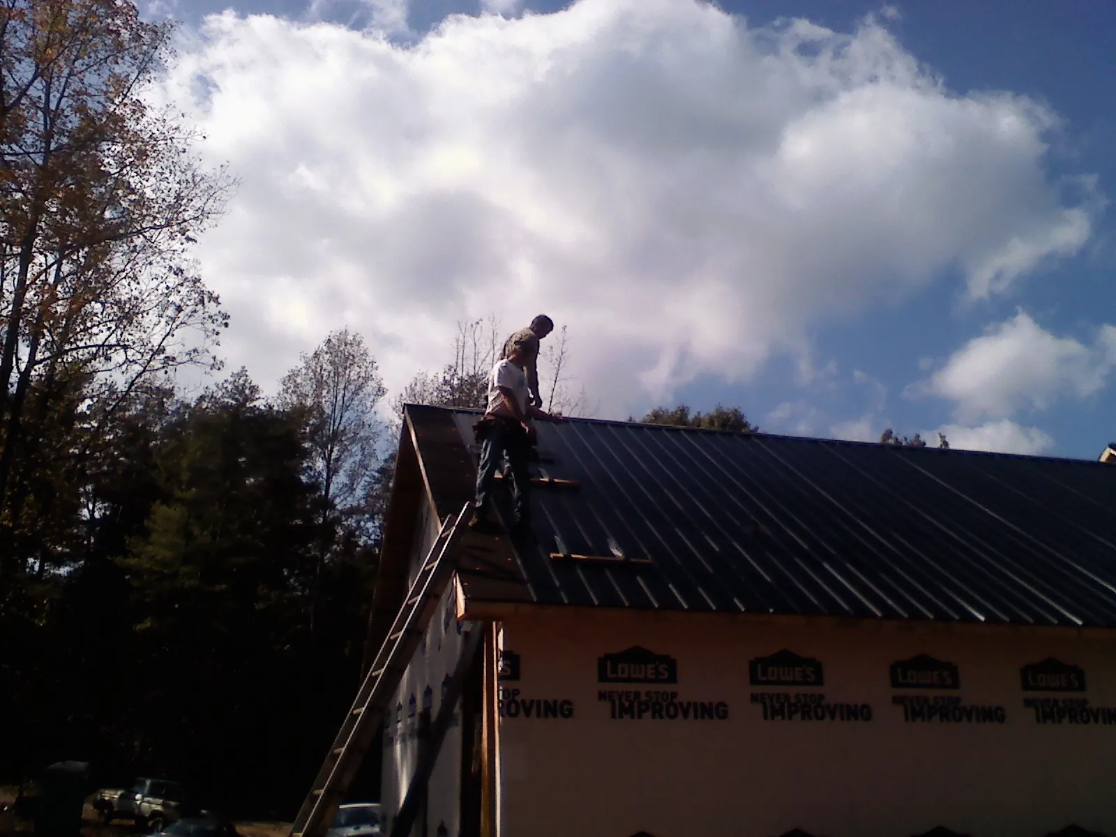 Roofer fastening dark metal panels high against a cloudy sky, from a Roof Inspection job in Beyer