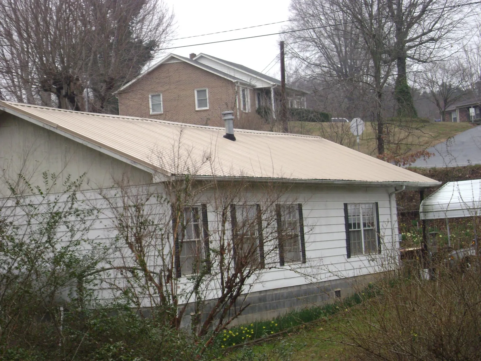 Tan metal roof on a white sided house set into a hillside — Commercial Roofing by Roofing Brothers in Beyer