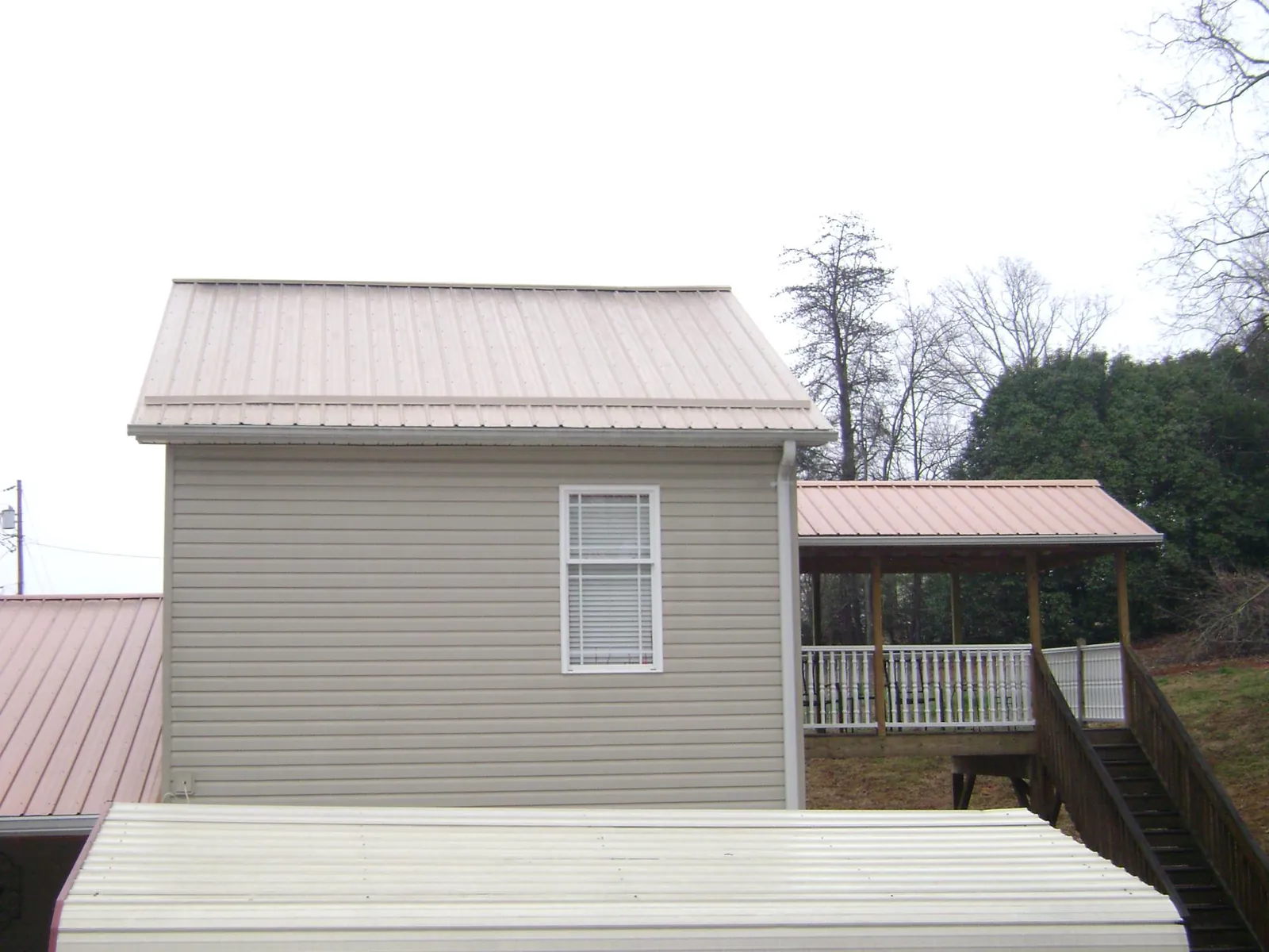 Tan metal roofs on a two story addition and attached porch, from a Roof Replacement job in Beyer